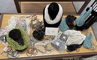 Wide view of all beaded necklaces laid out on table including white, black, green, blue and multicolor strands and bags of beads.