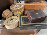 Group view of multiple vintage boxes and containers including wooden, fabric-covered, and woven basket styles, showing wear and unique designs.
