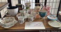 Photo of various vintage and collectible cups and mugs along with a handwritten lot number sign