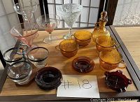 Photo showing the full lot contents arranged on a table including clear, pink, amber and red glass drinkware items.