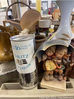 Photo of Schlitz bank, Hummel-style figurine, mustard yellow pitcher, other vintage ceramics and kitchenware.