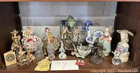 Shelf display with collection of various vintage figurines and bells showing assortment of ceramic and glass items.