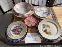 Display of vintage decorative plates and bowls with various floral and fruit motifs, arranged on a wooden surface under natural light.