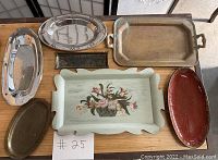 Seven vintage trays and platters displayed on a surface, showing a variety of materials and signs of wear.