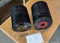 Two stacks of vintage 45 RPM vinyl records placed on metal stands, photographed from front-left angle, includes handwritten lot label #21.