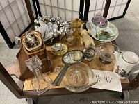 Overview of the assorted vintage collectible lot arranged on table including baskets, glassware, bells, and figurines.