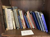 Books arranged on a wooden shelf showing various titles including The Kama Sutra, collectible dolls, and others, displaying wear and age.