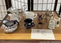Front angled view of 9 different vintage collectible creamers on a wooden table.