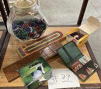 Lot displayed showing cribbage board, playing cards in wallets, poker chips in jar, fishing reel box, golf balls box.