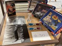 Overview of the James Dean poster, various racing collectible toy cars in packaging, 3D glasses, and an etched acrylic figure arranged on a table.