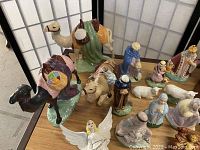 Porcelain nativity figurines arranged on a table, featuring camels, bull, shepherds, three wise men, and angel figurines visible.