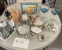 Photo of vintage ocean themed collectibles including lighthouse figurine, shells, votive holders, glassware, and framed art arranged on a round table.