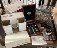 Photo showing three wine glasses in Petit Vin boxes, a wooden wine accessory box with four items, a large bag of used wine corks, and additional wine accessories.