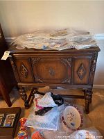 Front view of antique wooden sideboard showing carved door and detailed legs, items on top wrapped in bubble wrap not included
