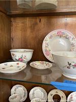 Shelf with various porcelain bowls and plates featuring floral patterns from Aynsley, Lefton, and others.