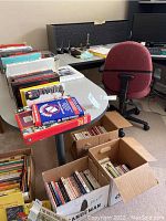 Photo of multiple books in cardboard boxes and a tabletop showing various book covers and spines.