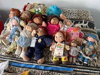 Photo showing 14 dolls primarily Cabbage Patch Kids and others arranged on fabric with animal print.