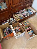 Photo showing multiple boxes and a dresser drawer filled with CDs, VHS tapes, DVDs, and cassettes.