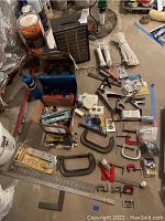 Lot of metal clamps, tools, hardware organizer, cords, torches and various hardware components spread on floor.
