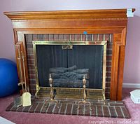 Front view of wood mantel with electric fireplace insert and brass mesh screen. Fireplace tools set displayed adjacent on hearth.