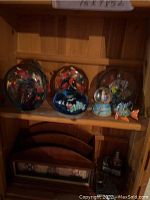 Shelf holding five colorful fish-shaped glass paperweights with detailed fish inside, a snow globe with a small ship inside, and a fish figurine.