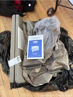 Disassembled taupe Graco Pack-N-Play fabric with accessories and frame components, placed on floor next to a white instruction manual.