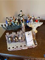 Three different menorahs grouped together on a table; includes ceramic textured stone wall menorah, white ceramic Star of David menorah, and a large metal menorah with colorful musical figurines.