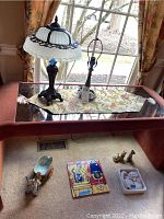 Table with two lamps on top and various figurines and wall tiles placed below on the floor.