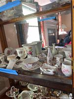 Shelf display with assorted Lefton and Limoges porcelain small plates, vases, and trinket boxes showing floral patterns and gold accents