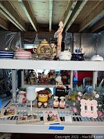 Two white shelves containing various decorative and collectible items such as music boxes, teapots, dolls, figurines, and candleholders.