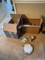 Two open boxes with bubble wrap, three dishware pieces on floor: a dinner plate, salad or dessert plate, and a mug cup with Snow Family design