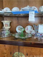 Assorted painted serving ware including Limoges plates, Stanley decorative glasses, green glass tiered serving tray, porcelain serving bowls and cake dome on wooden shelf