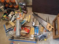 Full layout of painting supplies and hand tools including saws, towel rod, paint rollers, drop cloth and dryer installation kit scattered on concrete floor