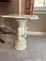 Side view of the pedestal table showing detailed carved base with cherub figures and ornamental accents