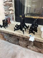 Photo displaying various black wooden plate holders arranged by size on a stone surface in front of a fireplace.