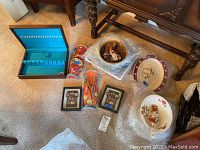 Multiple items including holiday serving dishes, collector plates, flatware box, ceramic vases, and framed art on carpeted floor