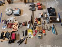 Wide view of assorted hand tools and small items including hooks, clamps, staple boxes, plane, and wrenches.