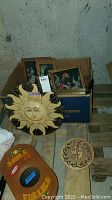 Overall view of the lot showing metal sun wall art pieces, framed dental ads in box, and wooden plaque