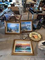 Overall lot photo including four framed nautical prints, Titanic life buoy mirror, nautical wall hanging and folded tapestries in basement setting.