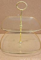 Two tier dessert stand showing gold rimmed clear glass plates and gold handle