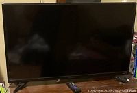 Front view of the black flat screen TV turned off, with remote placed in front.