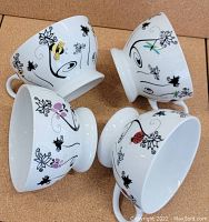 Four wide mouth white ceramic tea cups each decorated with whimsical bug designs and black vine patterns.