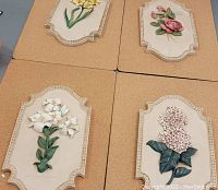 Four decorative floral wall plaquesset on a pedestrian folding table.