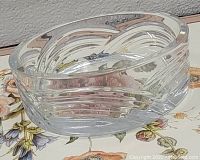 Clear glass candy dish with thick sides and angled decorative cuts photographed on a floral background.