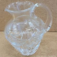 Front view of heavy crystal glassware creamer pitcher showing detailed pressed glass pattern, handle, and spout.