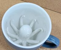 Top view inside of white ceramic mug showing the hidden sculpted octopus with eight tentacles extending from the center.
