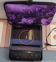 Copper Chef induction cooker front view with cover standing behind it, showing control panel and burner design.