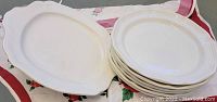 Photo showing several oval serving platters and stacked round plates with scalloped edges and embossed detailing in white porcelain.