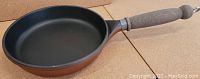 Photo of a small non-stick fry pan/skillet with a wooden handle showing black interior cooking surface and brown exterior.