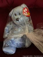 Light blue plush Ty Beanie Baby Clubby 2 bear sealed in clear plastic wrapping, seated on red background. Heart-shaped Ty tag attached to ear visible.